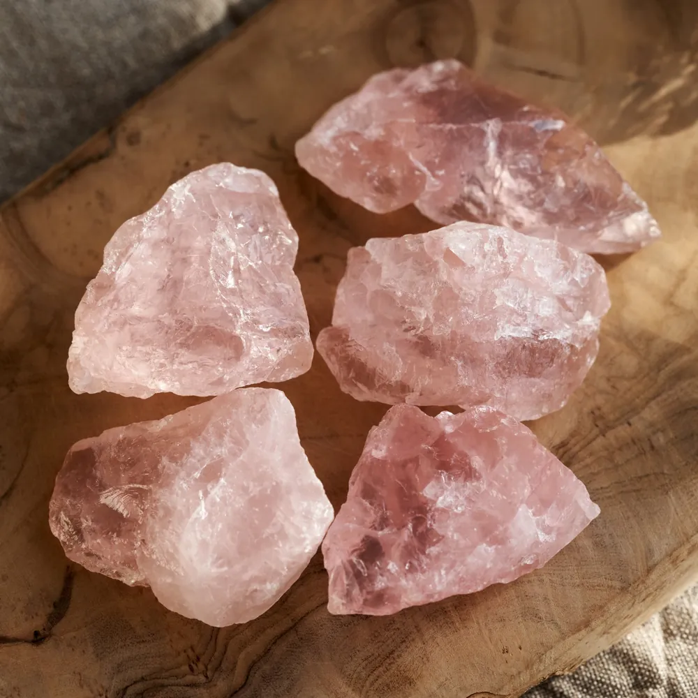 Cinq morceaux bruts de quartz rose posés sur du bois, pierre associée au chakra du cœur